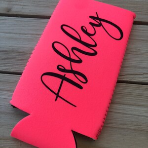 May include: A bright pink neoprene can cooler with the name "Ashley" printed in black.
