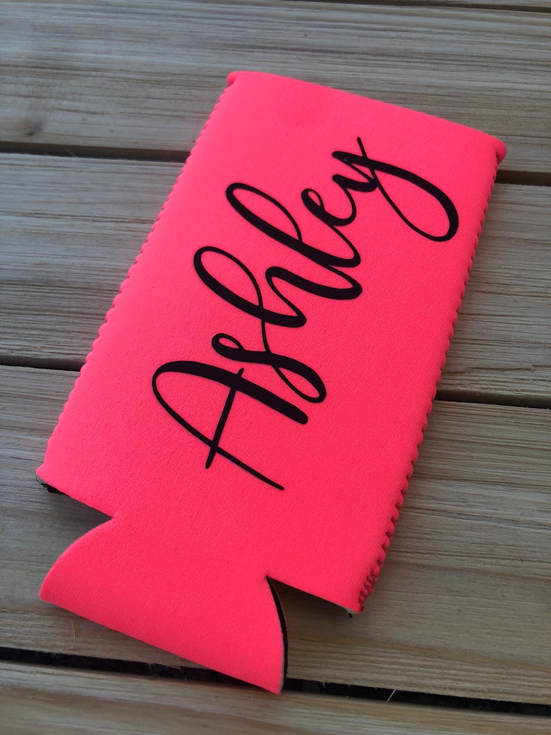 May include: A bright pink neoprene can cooler with the name "Ashley" printed in black.
