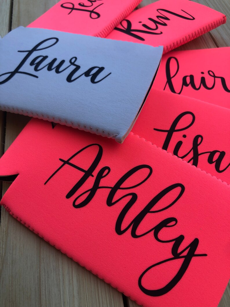 May include: A close-up of six personalized pink and light blue neoprene can coolers with names written in black. The names are Laura, Kim, Blair, Lisa, and Ashley.