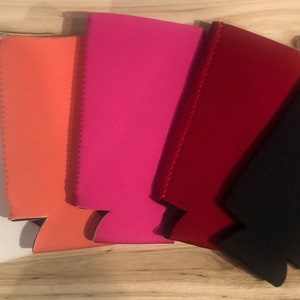 May include: Five neoprene can coolers in different colors: white, orange, pink, red, and black. The coolers are designed to keep drinks cold.