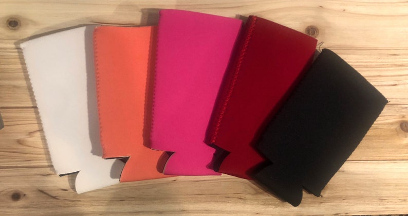 May include: Five neoprene can coolers in different colors: white, orange, pink, red, and black. The coolers are designed to keep drinks cold.