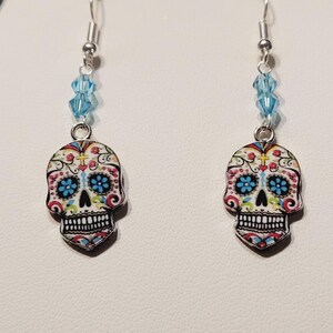 May include: A pair of silver dangle earrings with a sugar skull design and blue crystal accents.
