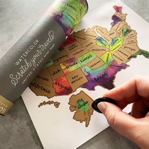 May include: A watercolor scratch-off map of the United States. The map is gold with colorful watercolor accents. The map is rolled up in a tube with the words "Watercolor Scratch Your Travels United States Mini Map" printed on the tube.