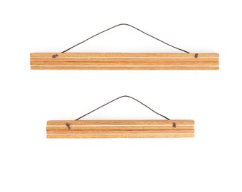 May include: Two wooden poster hangers with a natural wood grain finish. Each hanger consists of two wooden strips connected by a thin, dark string for hanging. The design is simple and minimalist, suitable for displaying artwork or posters.