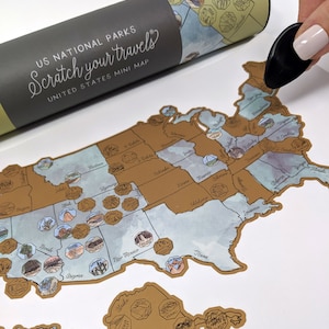 May include: A gold and brown scratch-off map of the United States featuring the names of each state and icons representing national parks. The text "US National Parks Scratch Your Travels United States Mini Map" is printed on the top of the map.