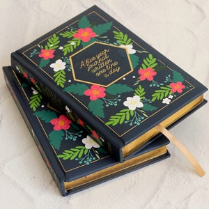 May include: Two navy blue journals with gold accents and a floral design. The top journal has the text "A five year journal written one line a day" on the front cover.