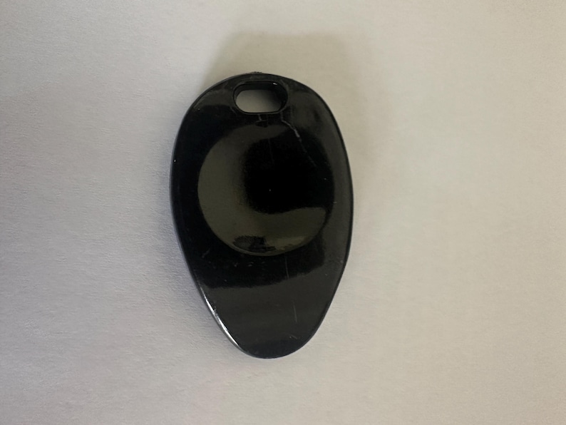 Pode incluir: Um objeto preto brilhante em forma oval com um pequeno orif&iacute;cio na parte superior. O objeto tem uma superf&iacute;cie lisa e reflexiva e uma forma ligeiramente alongada. O design &eacute; simples e minimalista.