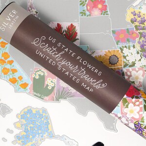 May include: A rolled up scratch-off map of the United States with each state illustrated with its state flower. The map is labeled "US State Flowers Scratch Your Travels United States Map".