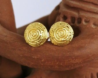 May include: A pair of gold-toned earrings with a circular design featuring a spiral pattern. The earrings are small and delicate.