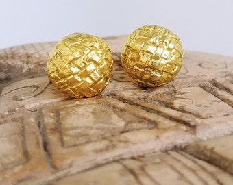 May include: A pair of gold-toned earrings with a woven texture. The earrings are round and have a slightly textured surface.