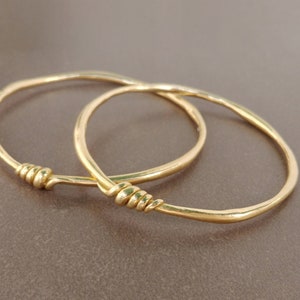 A handmade 18k solid gold asymmetrical bracelet crafted and designed with a small delicate decoration made of gold wire.