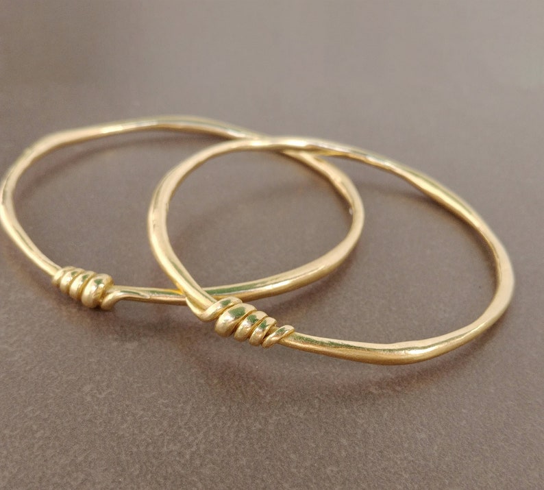 A handmade 18k solid gold asymmetrical bracelet crafted and designed with a small delicate decoration made of gold wire.