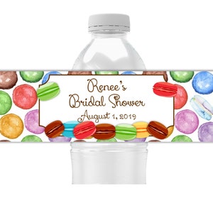 May include: A water bottle with a decorative label featuring a pattern of colorful macarons. The label includes the text "Renee's Bridal Shower August 1, 2019" in a brown script font, with a white background.