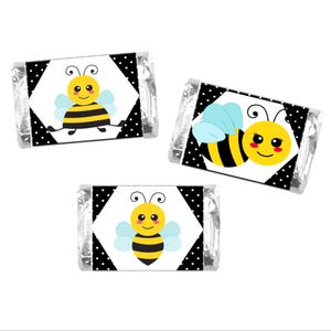May include: Three individually wrapped candies with bee-themed designs. Each candy wrapper features a black and white polka dot pattern with a white diamond in the center. The diamond contains a cartoon bee with yellow, black, and blue accents.