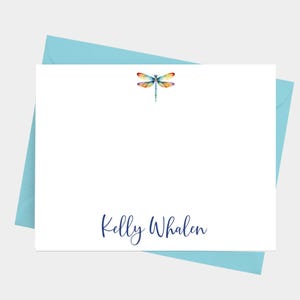 May include: A white stationery card with a colorful dragonfly illustration and the text "Kelly Whalen" in navy blue script.