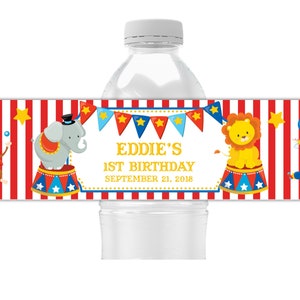 May include: Red and white striped water bottle label with a circus theme. It features a monkey juggling balls, an elephant on a platform, a lion on a platform, and a clown juggling balloons. The text reads "Eddie's 1st Birthday September 21, 2018".