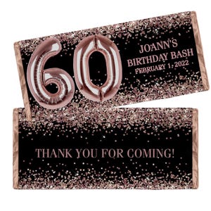 May include: Two chocolate bar wrappers with a black background and rose gold accents. One wrapper has the number 60 in rose gold balloon font. The other wrapper says "Thank you for coming!" and "Joann's Birthday Bash February 1, 2022."