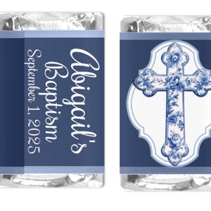 Può includere: Due barrette di cioccolato avvolte in carta stagnola. Una presenta il testo "Battesimo di Abigail 1 settembre 2025" in bianco su sfondo blu navy. L'altra presenta un disegno a croce floreale blu.