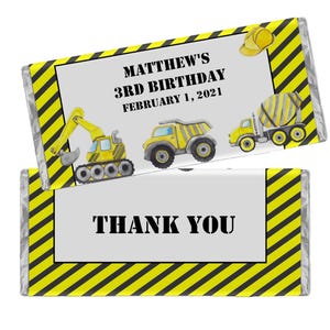 May include: Two candy bar wrappers with construction-themed graphics. One wrapper reads "MATTHEW'S 3RD BIRTHDAY FEBRUARY 1, 2021" and features illustrations of construction vehicles. The other wrapper says "THANK YOU". Both have yellow and black hazard stripes.