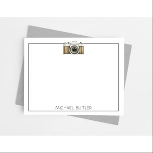May include: A white and brown camera illustration on a white card with a black border. The card has the text "MICHAEL BUTLER" at the bottom.