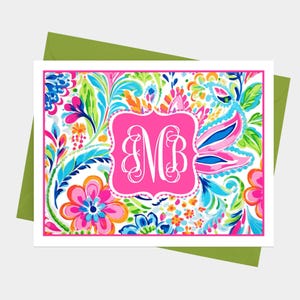 May include: A white card with a pink floral pattern and a pink monogram with the letters "MB" in the center. The card has a green envelope.