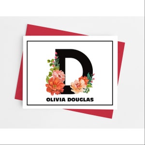 May include: A personalized stationery card featuring a large black letter "D" adorned with watercolor flowers in shades of orange and pink. The name "OLIVIA DOUGLAS" is printed below the letter. The card is set against a white background and a red envelope.