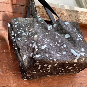 May include: A large black and white tote bag with a spotted pattern. The bag has black leather handles.