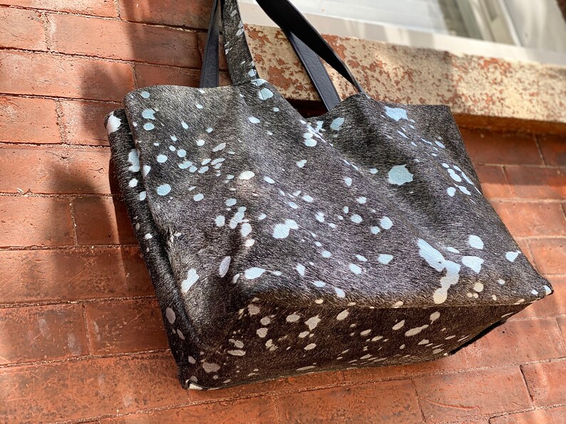 May include: A large black and white tote bag with a spotted pattern. The bag has black leather handles.