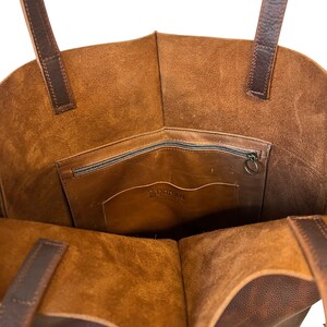 May include: A brown leather tote bag with a zippered pocket and a small interior pocket. The bag has a brown leather logo that says "URDAN" on the interior pocket.
