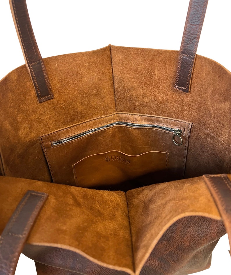 May include: A brown leather tote bag with a zippered pocket and a small interior pocket. The bag has a brown leather logo that says "URDAN" on the interior pocket.