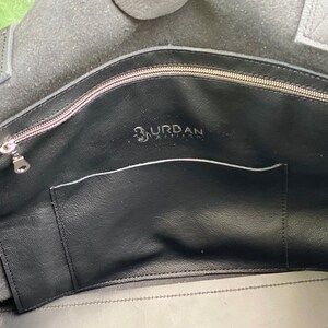 May include: The inside of a black leather tote bag with a zippered pocket and a smaller pocket. The bag has the text "Urban Artisan" printed on the inside.