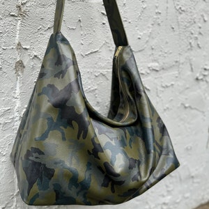 May include: A green, black, and brown camouflage print leather shoulder bag with a zipper closure.
