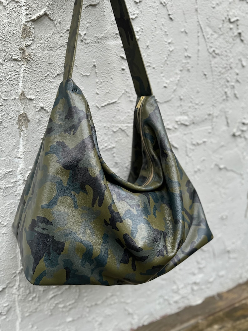 May include: A green, black, and brown camouflage print leather shoulder bag with a zipper closure.