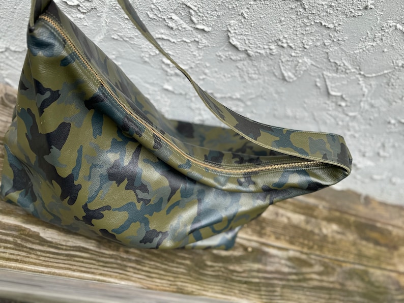 May include: A green, black, and blue camouflage leather shoulder bag with a gold zipper.