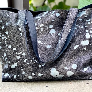 May include: A large black and white tote bag with a splatter pattern. The bag has two black leather straps.