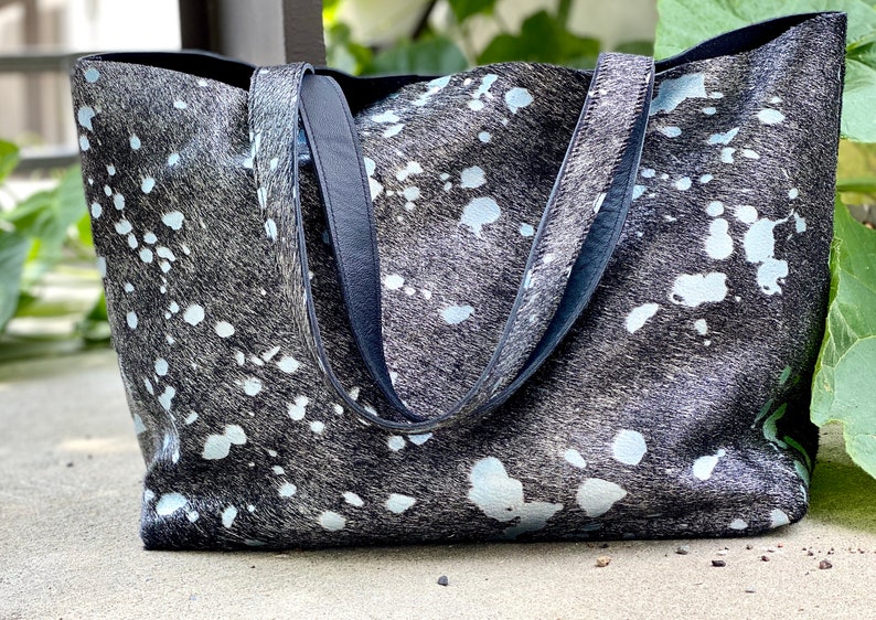 May include: A large black and white tote bag with a splatter pattern. The bag has two black leather straps.