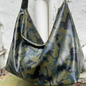 May include: A green, black, and blue camouflage print leather tote bag with a long shoulder strap.