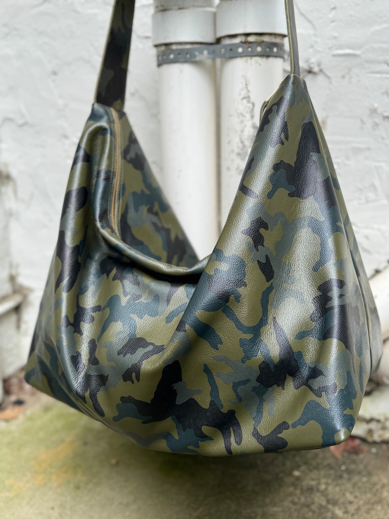 May include: A green, black, and blue camouflage print leather tote bag with a long shoulder strap.
