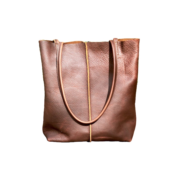 May include: A brown leather tote bag with a tan leather trim. The bag has two straps and a wide opening.