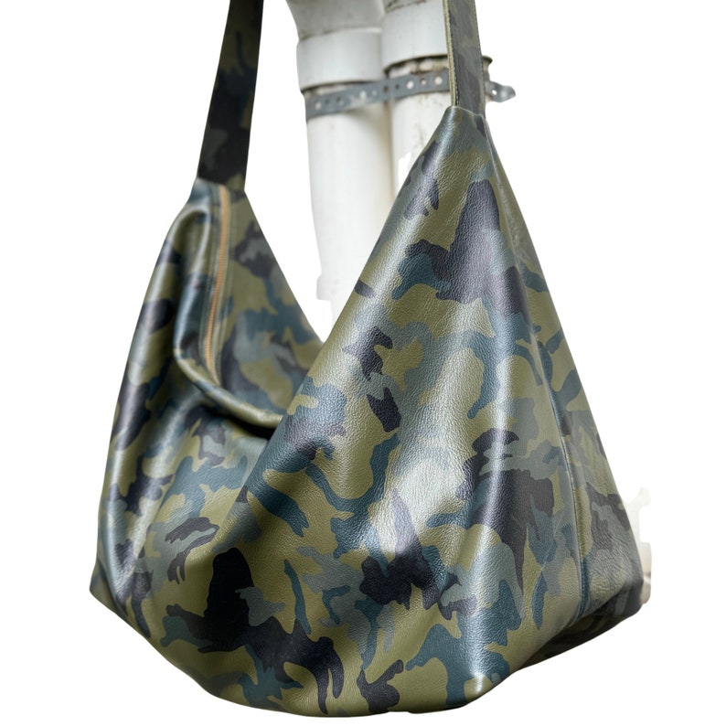 May include: A green and black camouflage print hobo bag with a long shoulder strap.