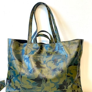 May include: A large tote bag with a camouflage pattern in shades of green, blue, and black. The bag has two long handles and a front pocket. The bag is made of a textured material.