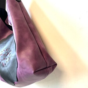 Puede incluir: Un bolso tote de cuero morado con un acento de cuero negro y un dise&ntilde;o recortado. El bolso tiene una sola correa.