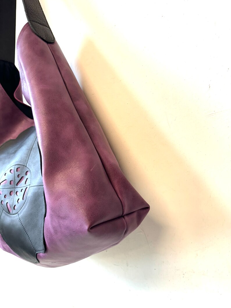 Puede incluir: Un bolso tote de cuero morado con un acento de cuero negro y un dise&ntilde;o recortado. El bolso tiene una sola correa.