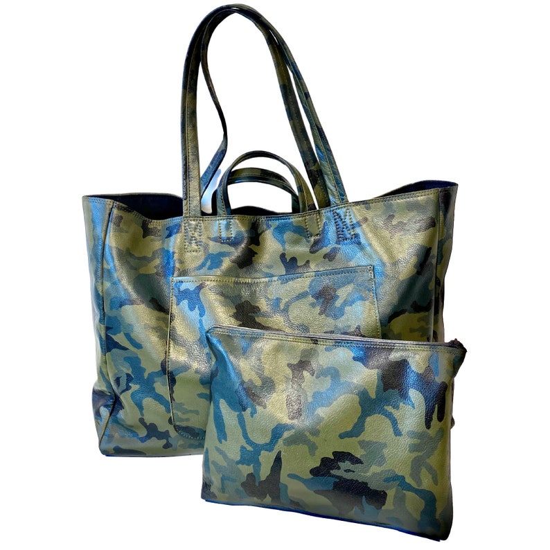 May include: A large tote bag and a smaller pouch, both featuring a camouflage pattern in shades of green, blue, and black. The tote has long handles and a front pocket. The pouch has a zipper closure.