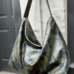 May include: A large, green, black, and blue camouflage-patterned leather tote bag with a long shoulder strap.