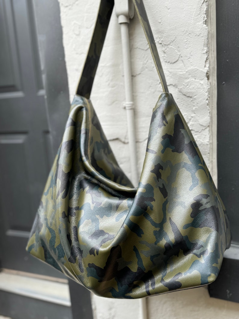 May include: A large, green, black, and blue camouflage-patterned leather tote bag with a long shoulder strap.