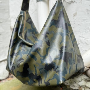 May include: A green, black, and blue camouflage-patterned leather shoulder bag. The bag has a long strap and a zipper closure.