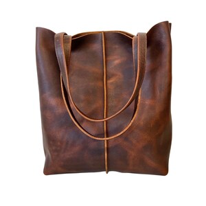 May include: A brown leather tote bag with two straps. The bag has a distressed look and a light brown stitching detail.