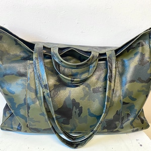 May include: Large tote bag with a camouflage pattern in shades of green, black, and brown. The bag has two handles and a spacious interior. The bag is made of a textured material.