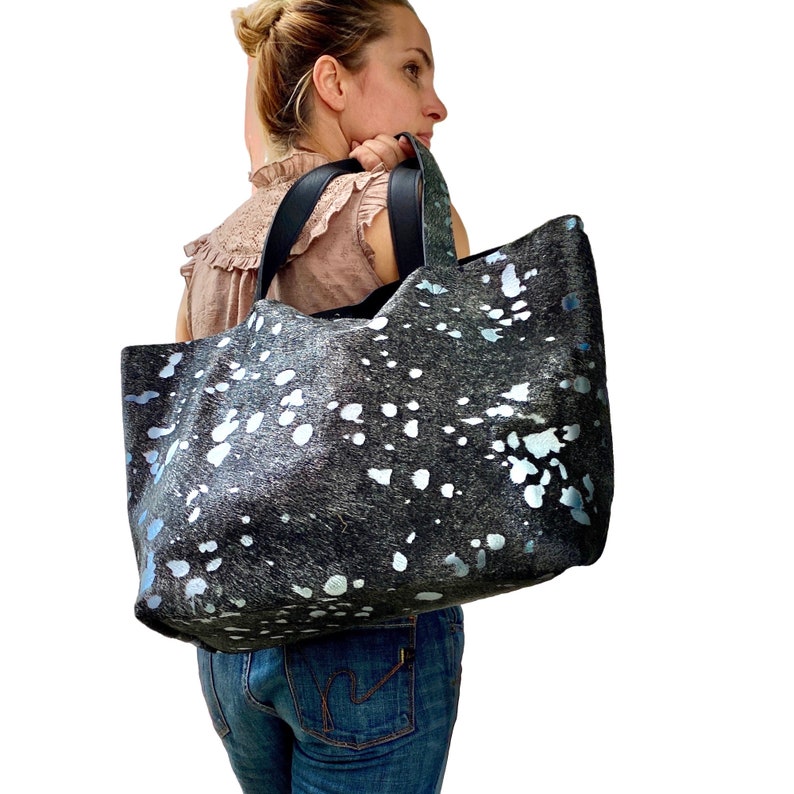 May include: A large black and white tote bag with silver accents. The bag is made of leather and has a spotted pattern.